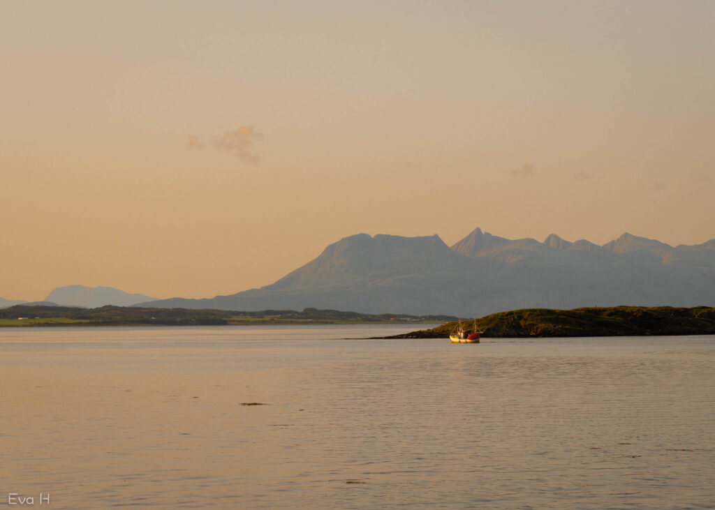 Gul/orange lys i solnedgangen . Hav, holmer og en enslig fiskebåt på vei mot vest. De sju søstrene i bakgrunnen. Fargebilde. Fotografi.