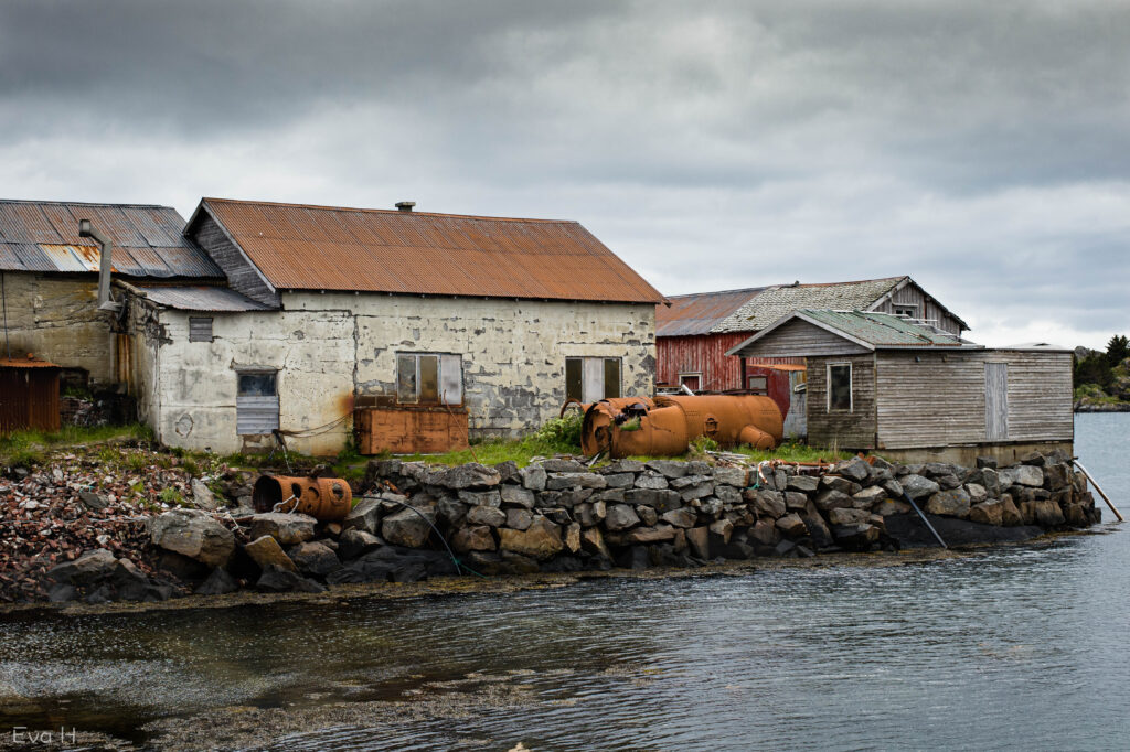 Rustne tak og tanker, og avskallet maling på murveggene i et lite fiskevær et sted i Nord-Norge. Fargebilde. Fotografi.