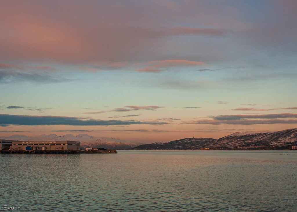 Rosa skjær over himmelen og fjellene i sør. Snøvinter ved Tromsøsundet. Fargebilde. Fotografi.