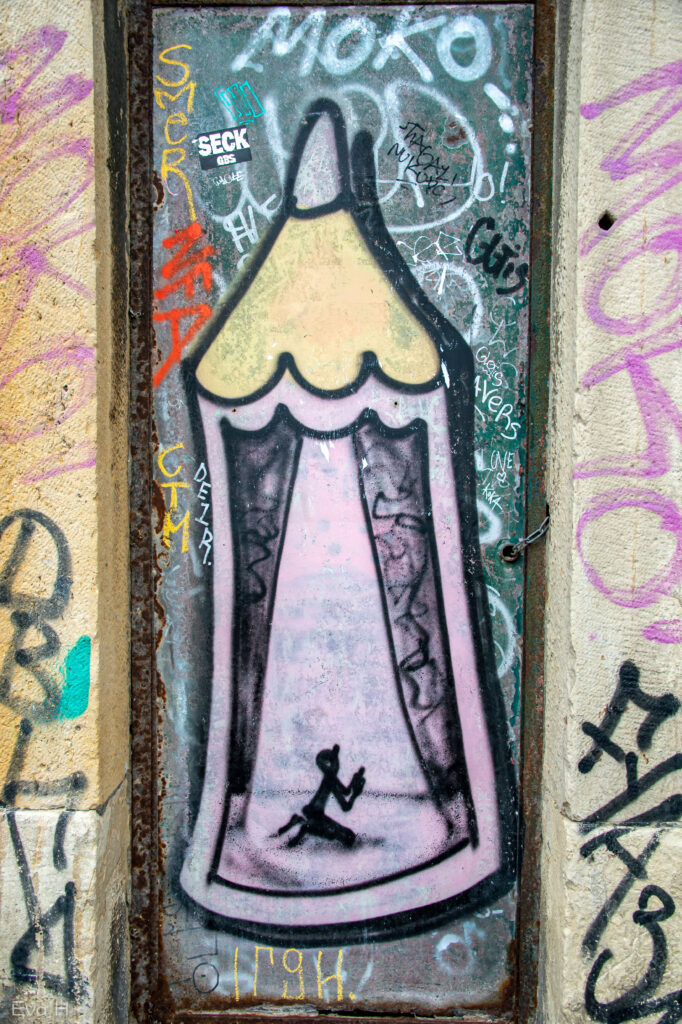 Lilla blyant med liten knelende mannsfigur på vegg med grafitti. Gatekunst. Lisboa. Fotografi