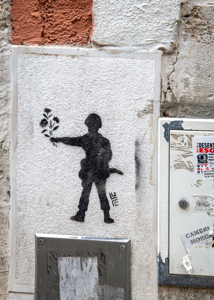 Svart soldatfigur strekker fram en blomsterbukett. Lisboa. Gatekunst. Fotografi