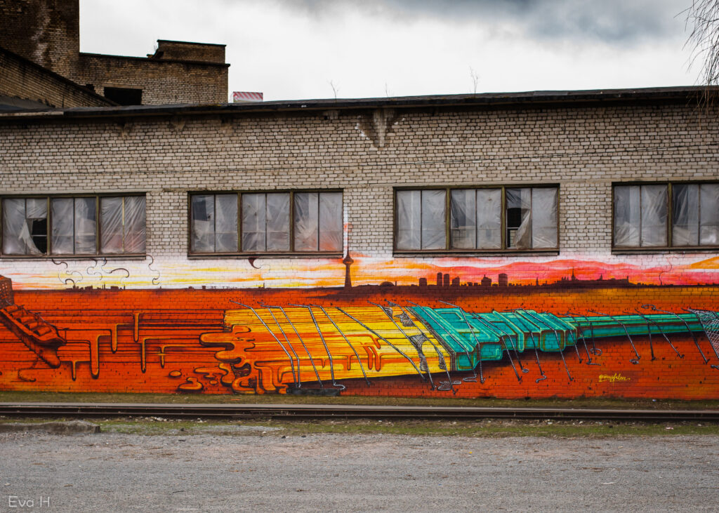 Gråvær i Tallin. Fargerik malerpensel bundet fast til muren. Storbysilhuett i bakgrunnen. Malt på murveggen. Fotografi av gatekunst