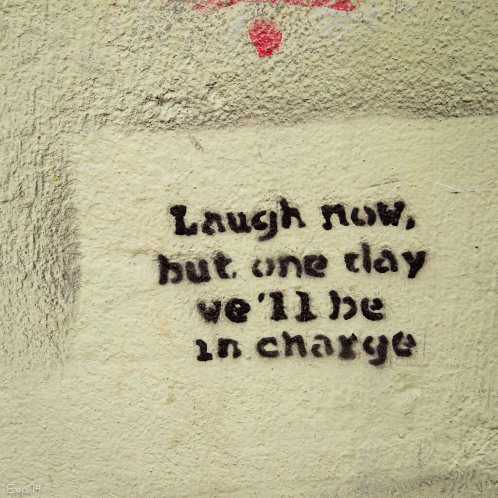 Tekst på grov murvegg: Laugh now, but one day we'll be in charge. Fotografi av gatekunst