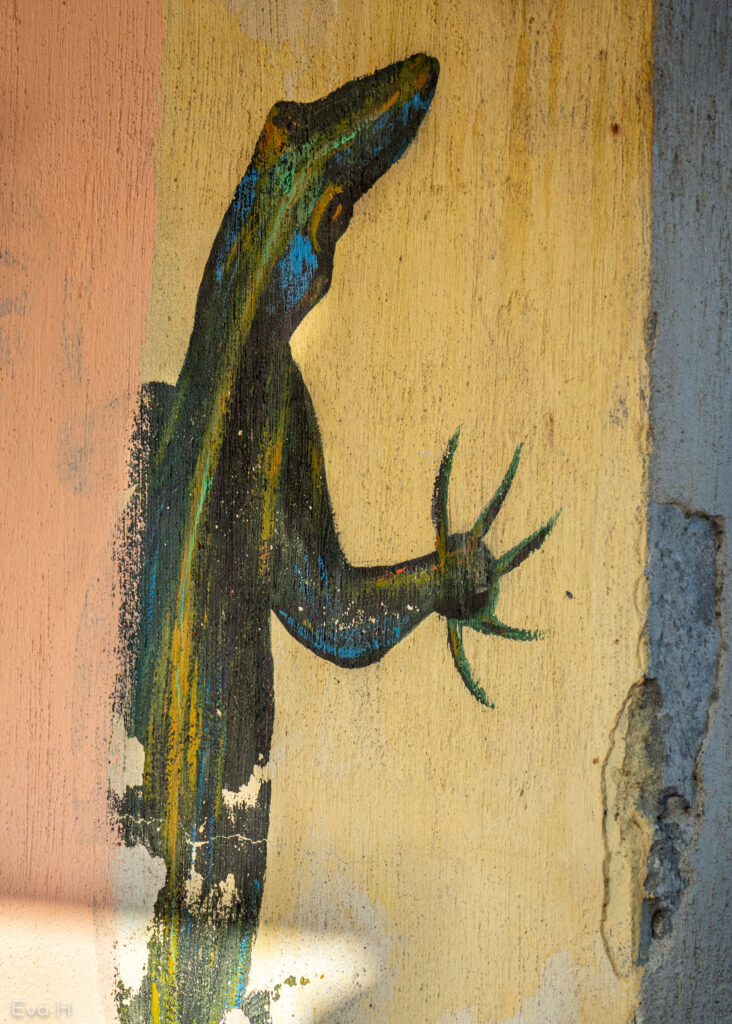 Delvis ødelagt maleri av firfisle på en murvegg. Grønn, gul, litt blå. Fotografi av gatekunst