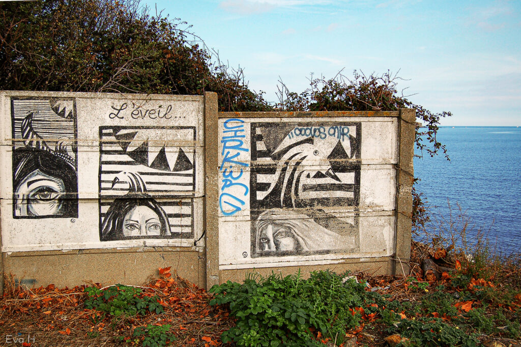 Sort/hvitt- malerier på mur med havet bak. Fotografi av gatekunst