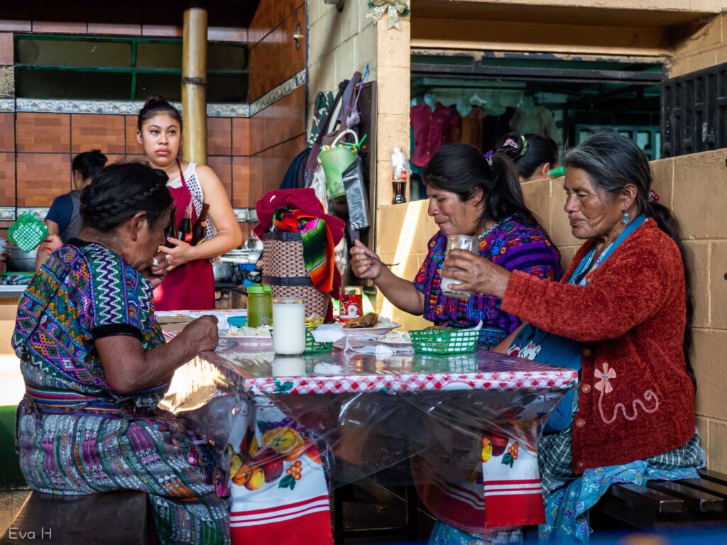 Mayakvinner spiser lunsj på innendørs-marked. Fargefotografi